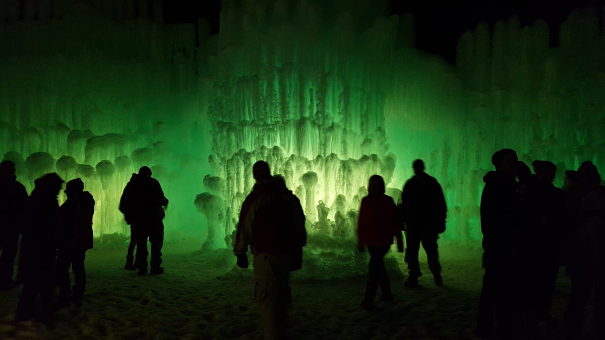 People walking around the ice castle with green lighting