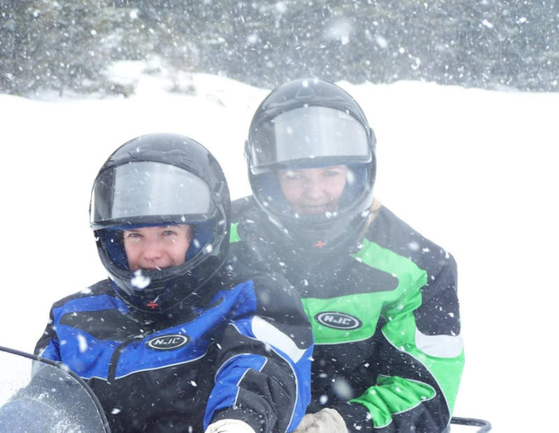 Two people on a snowmobile in snowy weather.